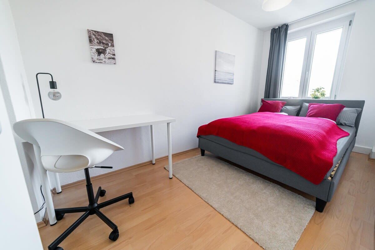 Un dormitorio con cama, escritorio, silla y ventana.