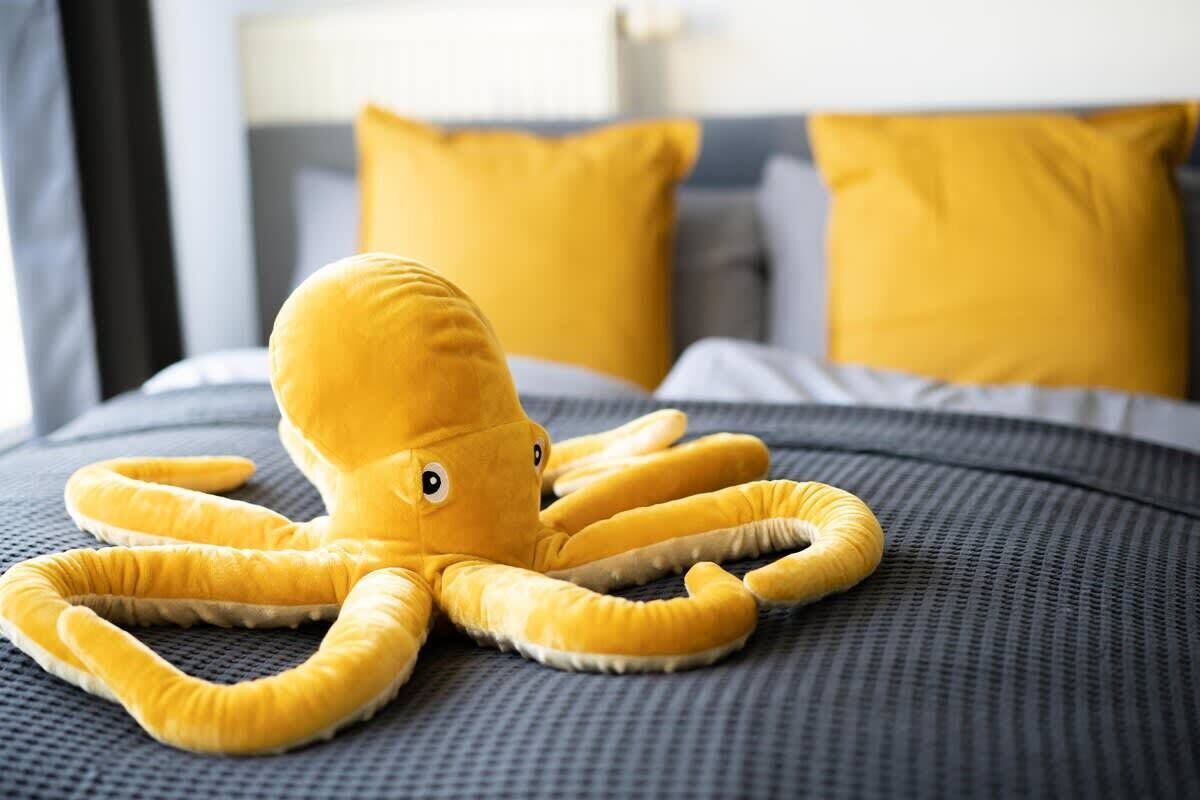 A plush octopus toy on a bed with a grey and yellow color scheme.