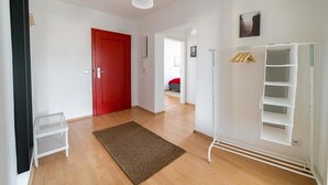 A hallway with a red door, a white shelving unit, and a brown rug. - FullHouse | Chemnitz | HS46 | 3 Bedroom (Chemnitz)