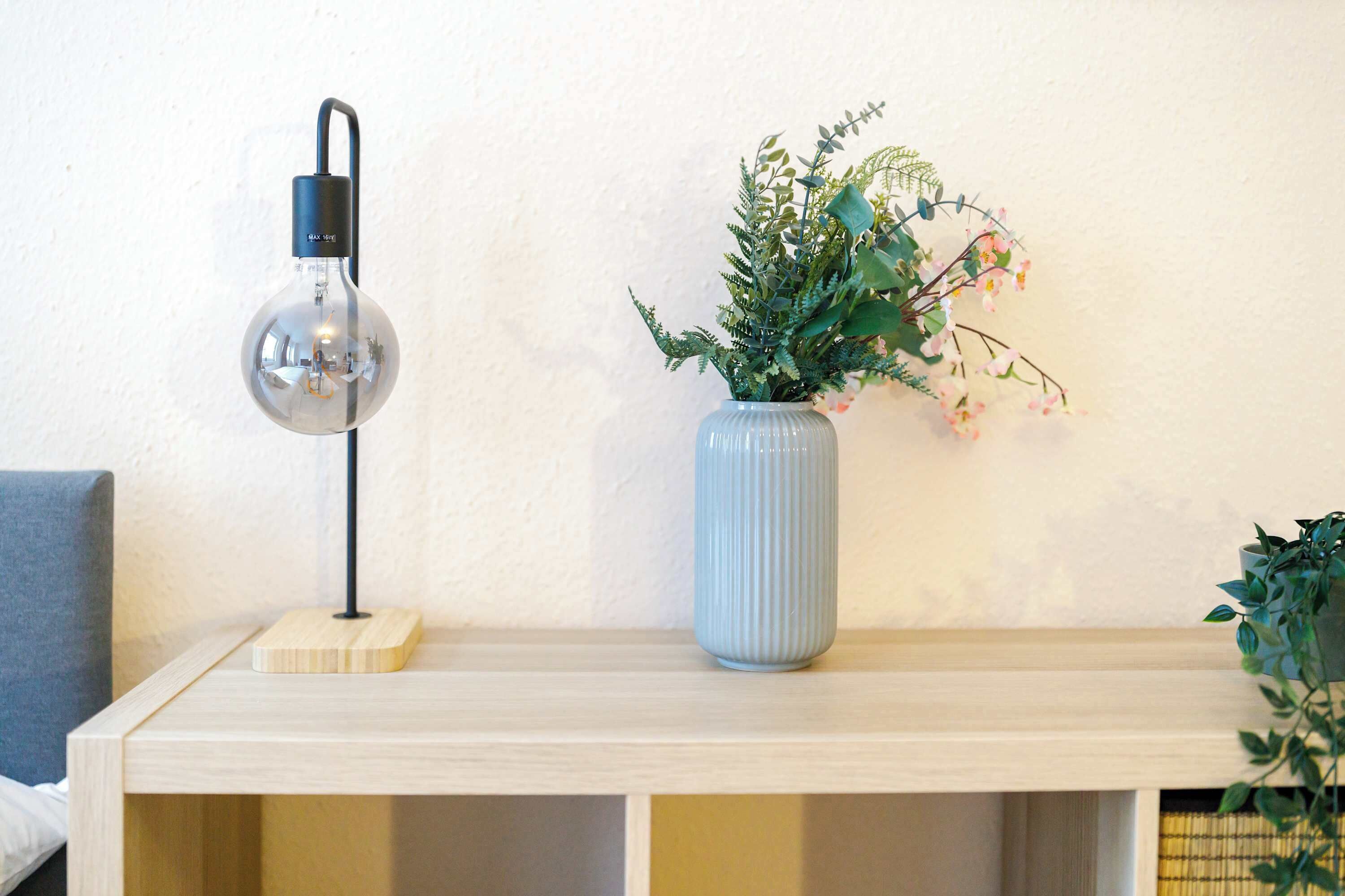 Une étagère en bois, une ampoule transparente et un vase bleu contenant des plantes vertes.