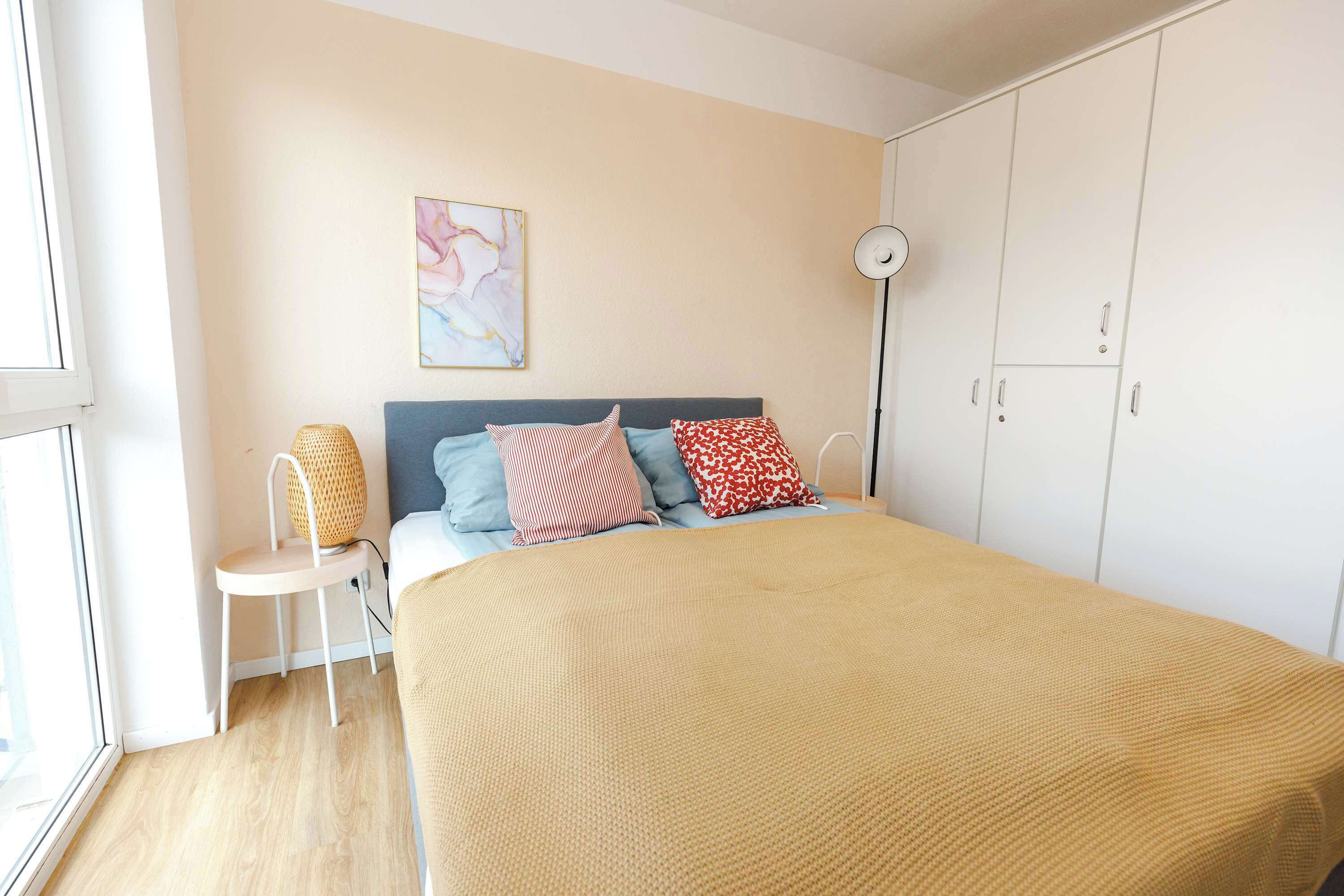 A bedroom with a bed, pillows, a chair, a floor lamp, and a wardrobe.