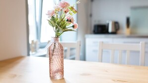 Ein Holztisch mit einer rosafarbenen, strukturierten Vase, gefüllt mit rosa Blumen.