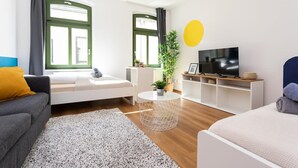 A modern living room with a sofa, a coffee table, a TV, and a large window with curtains. - FullHouse | Halle | R6 Amsterdam (Halle (Saale))