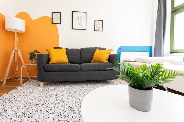 A modern living room with a grey sofa, yellow cushions, a white coffee table, a floor lamp, and a potted plant. - FullHouse | Halle | R6 Amsterdam (Halle (Saale))