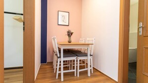 A small dining area with a wooden table and four white chairs, a vase with flowers, and a framed picture on the wall. - FullHouse | Halle | R6 Amsterdam (Halle (Saale))