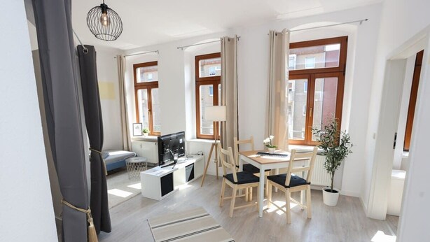 A modern living room with a sofa, TV, dining table, and chairs. - FullHouse | Chemnitz | M45-1 | Studio (Chemnitz)