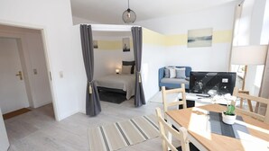 A modern, well-lit room with a bed, a desk with a computer, and a dining area with chairs and a table. - FullHouse | Chemnitz | M45-1 | Studio (Chemnitz)