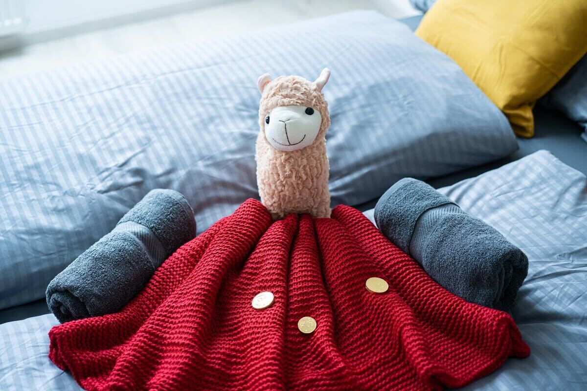 A bed with a red blanket, pillows, and a stuffed animal.