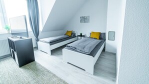 A modern bedroom with two single beds, a desk, and a window with curtains. - FullHouse | Magdeburg | L10-4 | Loft-Flair (Magdeburg)