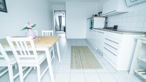 A modern kitchen with white cabinets, a wooden dining table, and chairs. - FullHouse | Magdeburg | L10-4 | Loft-Flair (Magdeburg)