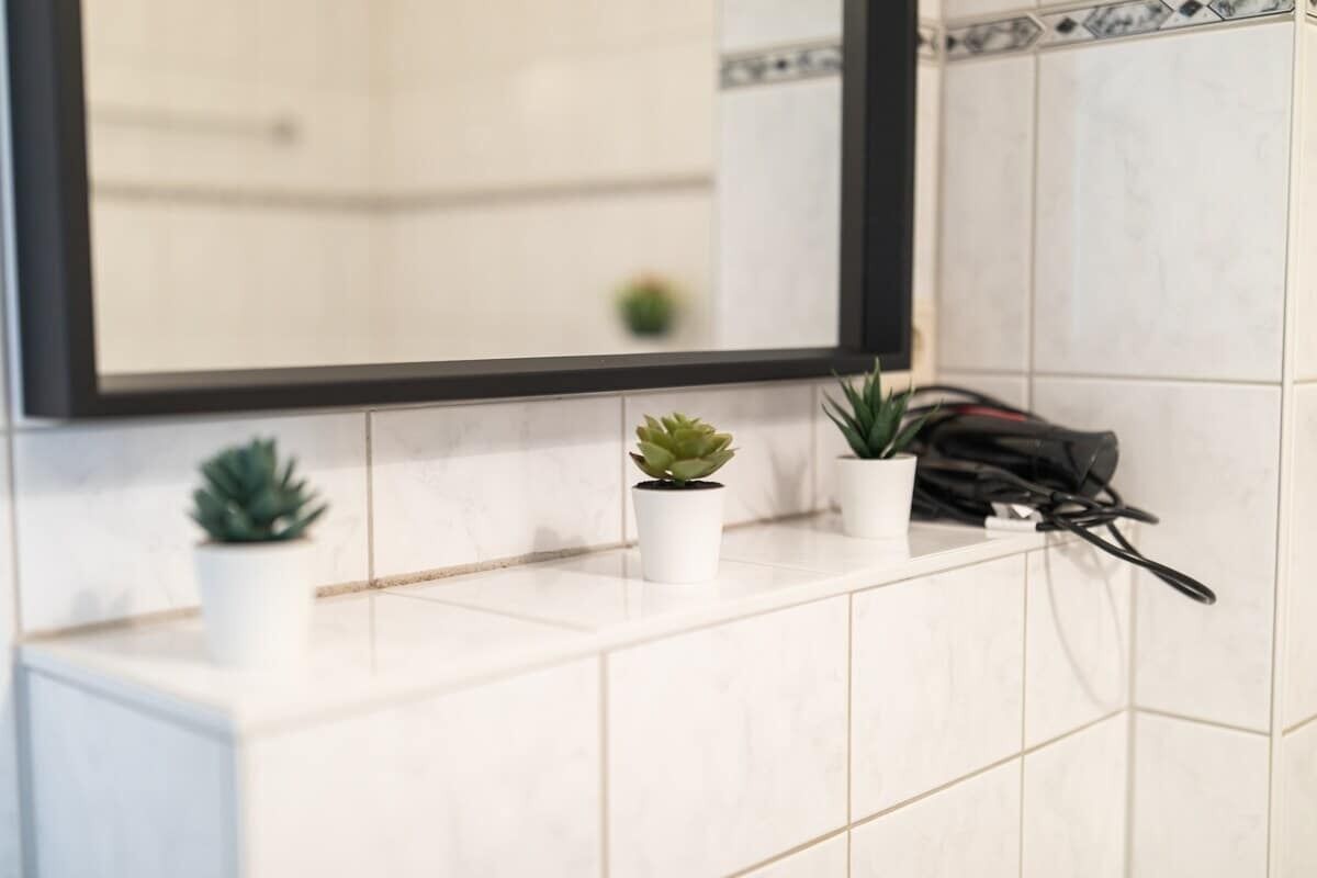 Un baño con azulejos blancos, un espejo y dos plantas en macetas sobre el mostrador.