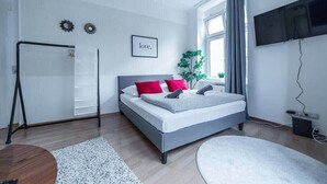 A modern bedroom with a bed, a TV, a window, and a plant. - FullHouse | M18-4 | Kings Palace (Erfurt)