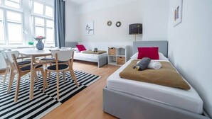 A modern, well-lit room with a bed, a small table with chairs, a sofa, and a window with curtains. - FullHouse | M18-4 | Kings Palace (Erfurt)