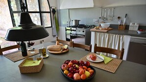Een keuken met een eettafel gedekt voor een maaltijd, met een schaal fruit, een fles wijn en een brood.
