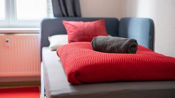 A neatly made bed with a red blanket and a folded gray towel.