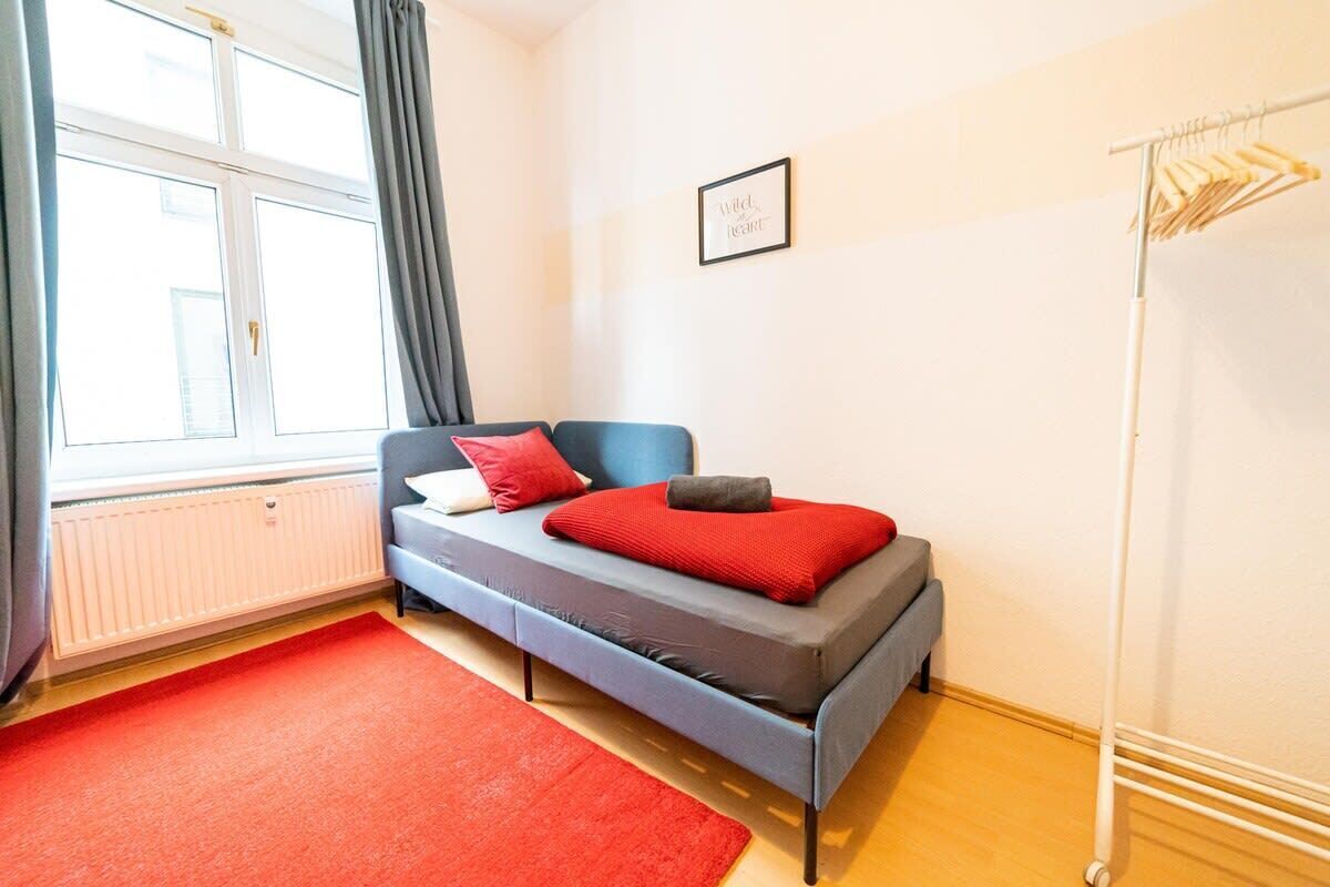 Ein modernes Schlafzimmer mit Bett, Heizkörper, einem Fenster mit Vorhängen und einem an der Wand befestigten Handtuchhalter.