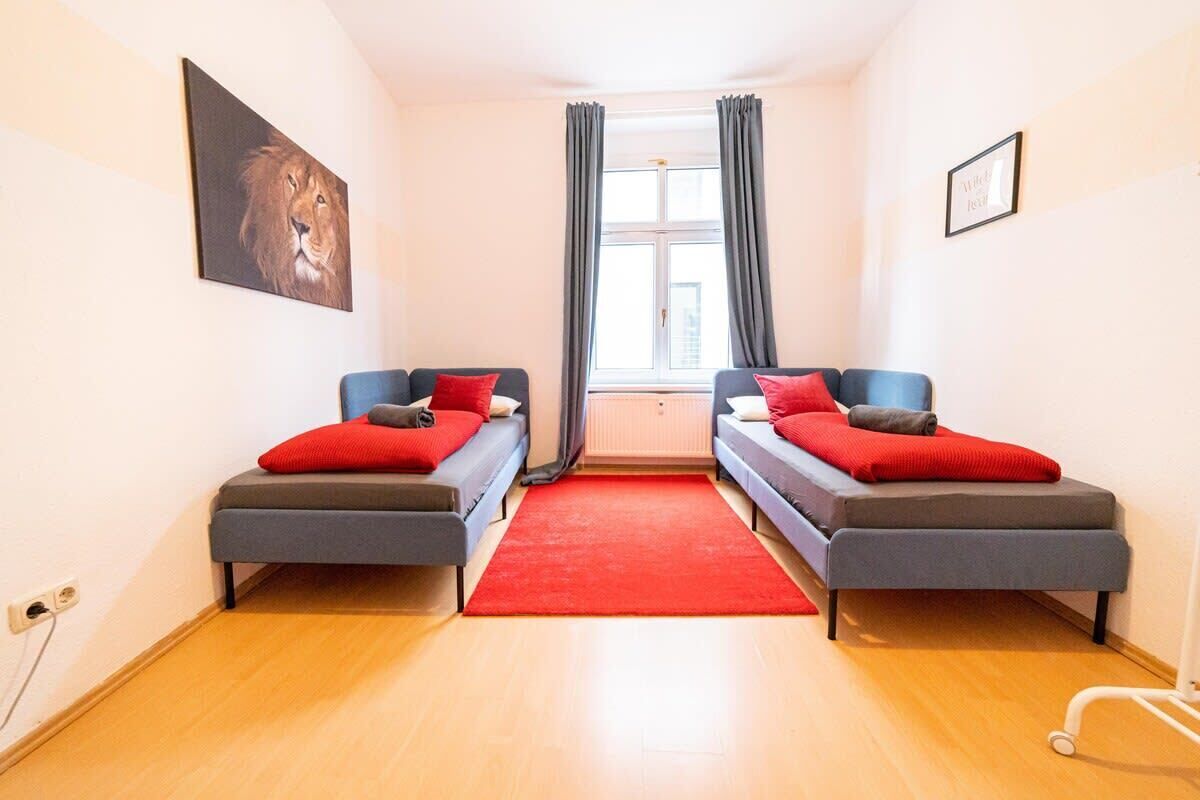 Ein Zimmer mit zwei Einzelbetten, einem roten Teppich, einem Fenster mit Vorhängen und einem Gemälde an der Wand.