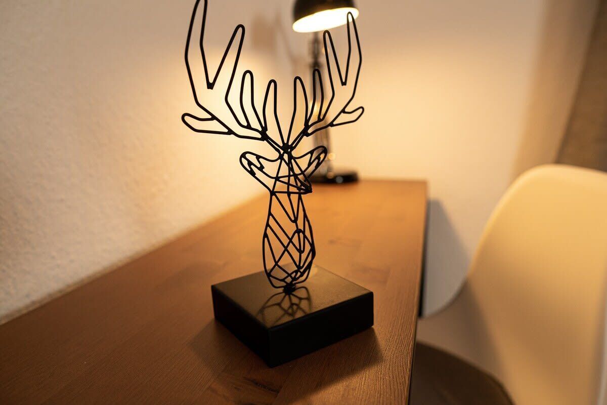 Een zwarte metalen sculptuur van een hertenhoofd op een houten tafel.