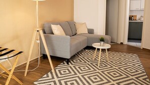 Ein Wohnzimmer mit grauem Sofa, einem kleinen runden Tisch, einer Lampe und einem gemusterten Teppich.