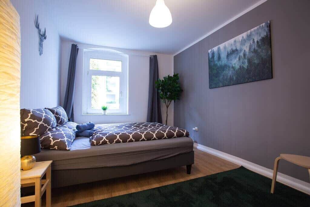 Un dormitorio con cama, ventana, un cuadro y una planta.