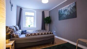 Un dormitorio con cama, ventana, un cuadro y una planta.