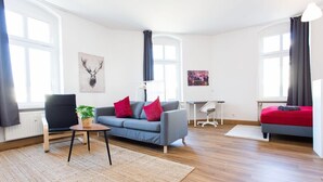 Una sala moderna con un sofá azul, una cama roja y una mesita con una planta.