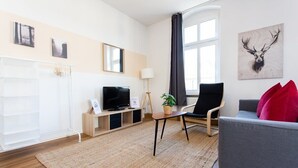 Una sala de estar moderna con televisión, un sofá, una silla y un ventanal grande.