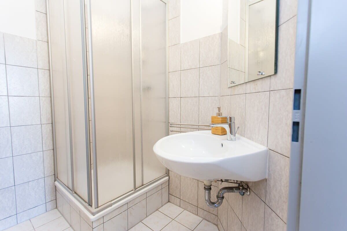 A modern bathroom with a glass shower enclosure, a white sink with a soap dispenser, and a mirror on the wall.
