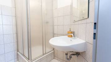 A modern bathroom with a glass shower enclosure, a white sink with a soap dispenser, and a mirror on the wall.
