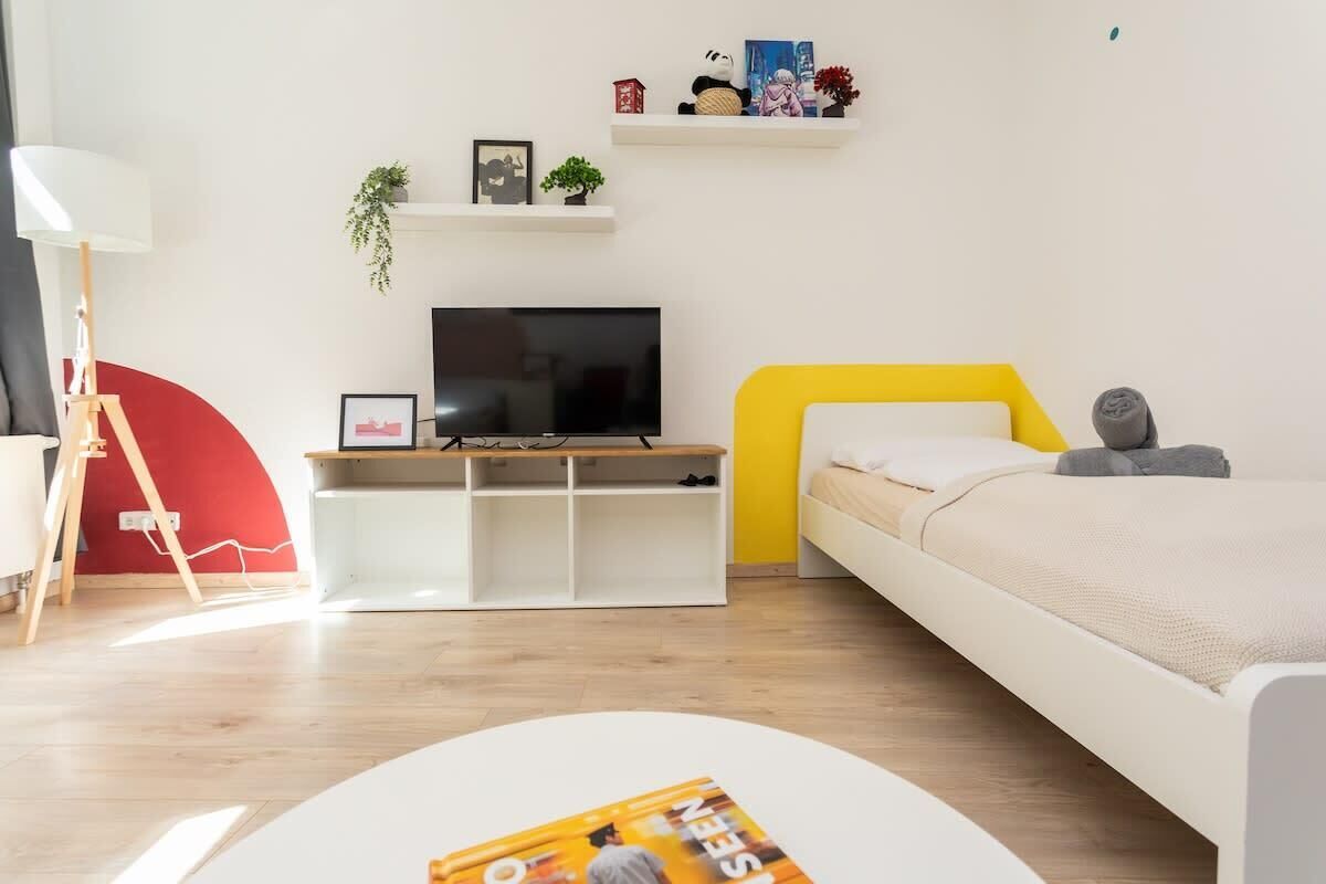 Une chambre à coucher moderne avec un lit, une télévision, une console blanche et un mur d’accent rouge.