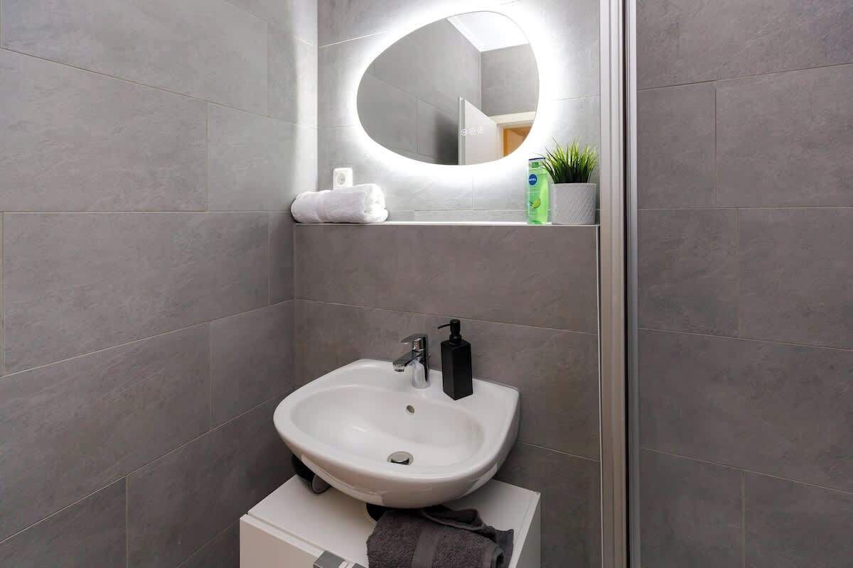 A modern bathroom with a white sink, a mirror with a light, and a towel rack.