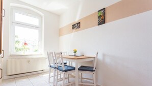 Een kamer met raam, radiator, tafel met stoelen en wanddecoratie.