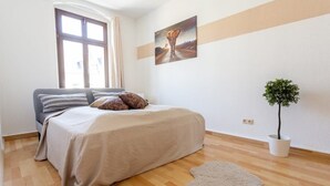 Een slaapkamer met een bed, een raam, een schilderij en een potplant.
