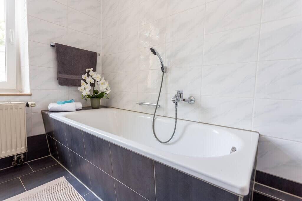 Un baño moderno con una bañera independiente, un perchero con toalla y un jarrón con flores.