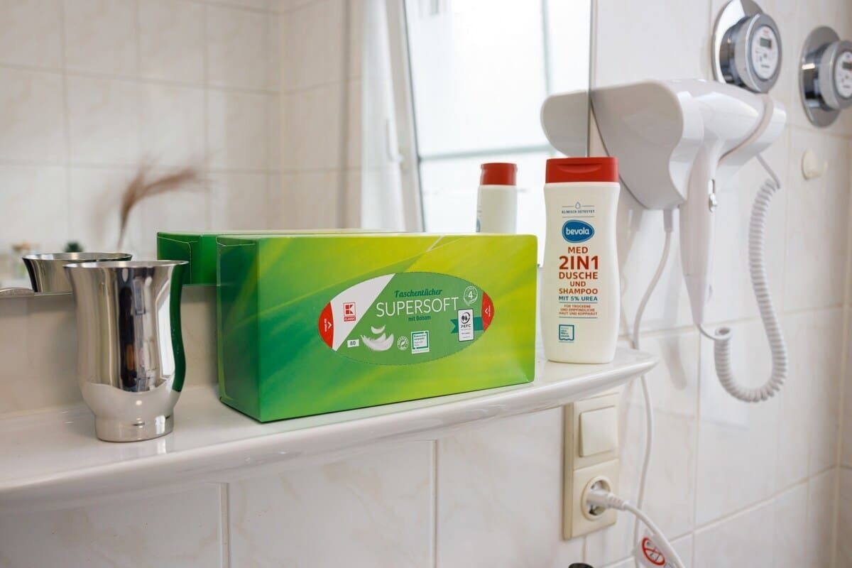 Een badkamer met een douche, een groene verpakking Supersoft shampoo en een witte fles Zini 1 shampoo.