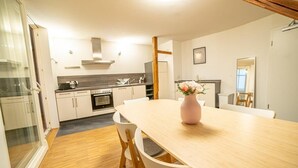 A modern kitchen with white cabinets, a wooden dining table, and a vase with flowers.