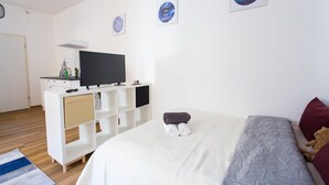 A bedroom with a bed, a TV on a white cabinet, and artwork on the wall. - FullHouse | Halle | T28 Hawk Apt. (Halle (Saale))
