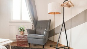 Une pièce avec un fauteuil gris, une lampe sur pied, une petite table avec une plante et un tapis noir.