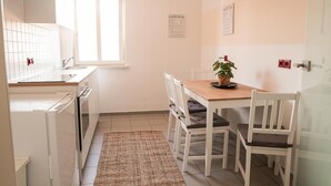 Une cuisine de taille réduite avec des meubles blancs, un plan de travail en bois, un évier et une fenêtre. On y trouve une table avec des chaises et une plante.