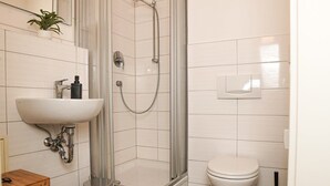 Une salle de bain équipée d’une douche, de toilettes, d’un lavabo et d’une petite table en bois.