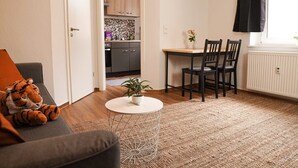 Un salon comprenant un canapé, une petite table ronde avec une plante, et un coin repas avec des chaises et une table.
