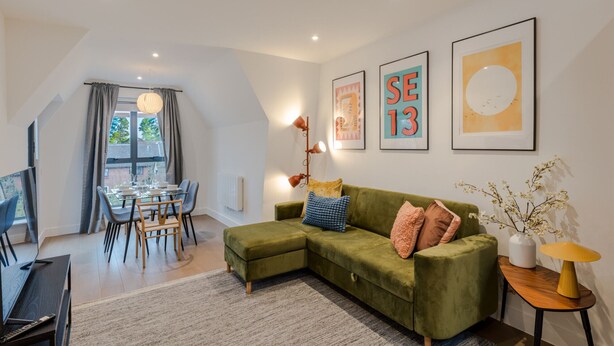 Een moderne woonkamer met een groene modulaire bank, een eethoek met een glazen tafel en kunstwerken aan de muren.