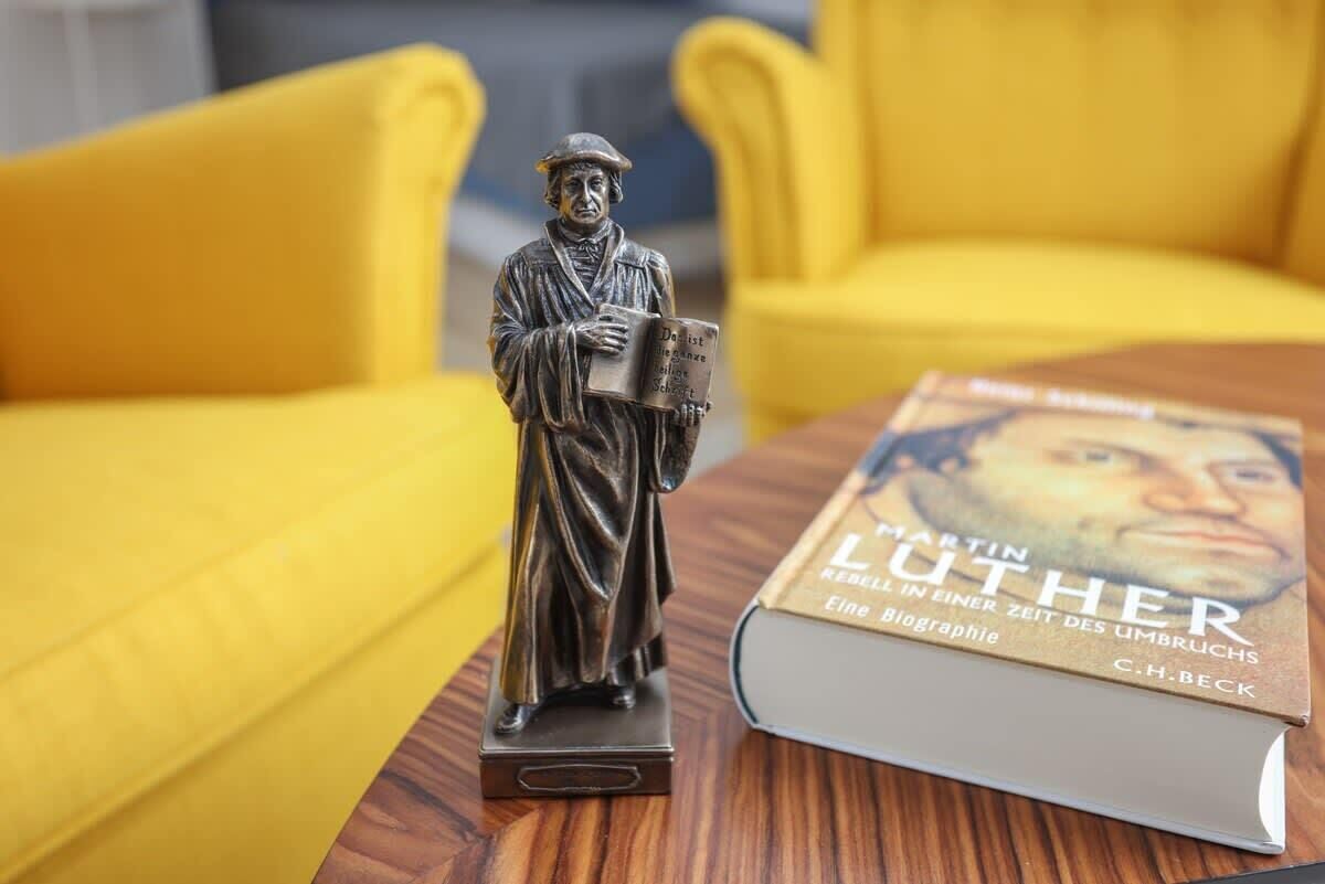 En staty av en historisk person som håller i en bok, placerad på ett träbord bredvid en bok med titeln ”Martin Luther”.