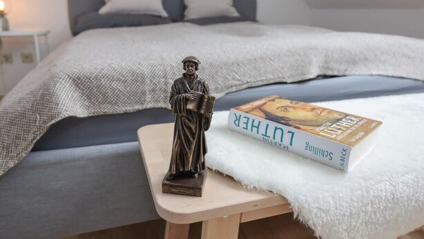 Un dormitorio con una cama, una mesita de noche con un libro y una estatua.