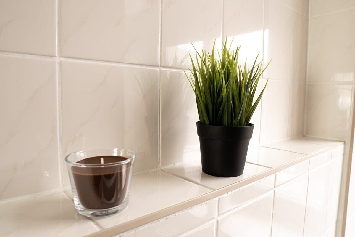 Een badkamer met witte tegels, een glazen kandelaar en een potplant.