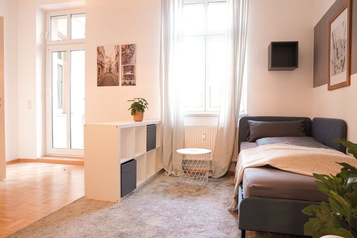 A bedroom with a bed, a small table, a radiator, and a window with curtains.