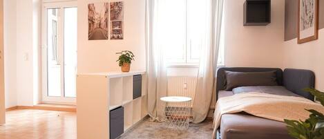 A bedroom with a bed, a small table, a radiator, and a window with curtains.