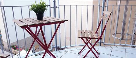 Ein Balkon mit Holztisch und Stuhl, einem Blumentopf und Blick auf ein Gebäude und einen Garten.