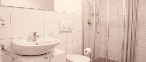 Un baño moderno con lavamanos blanco, inodoro y ducha con mampara de vidrio.
