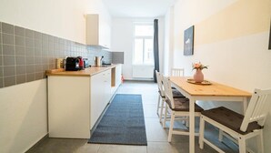 Una cocina compacta con comedor, que incluye una pequeña mesa y sillas, una cafetera y un ventanal con cortinas.